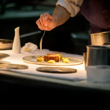 un chef préparant un plat avec de la viande éclairé par une lumière mettant en valeur son plat